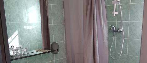 Un baño con un lavabo blanco, un armario de vidrio, una ducha con cortina y paredes con azulejos verdes.