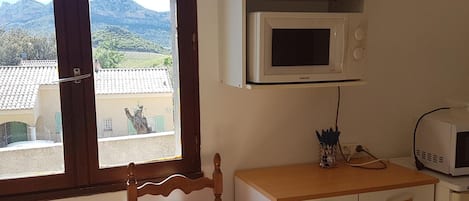 A room with a wooden chair, a desk with drawers, a microwave, and a view of a mountain landscape through a window.