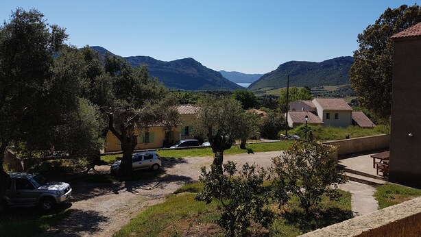 Paisagem rural com estrada de terra, carros estacionados e casas com telhados de cerâmica.