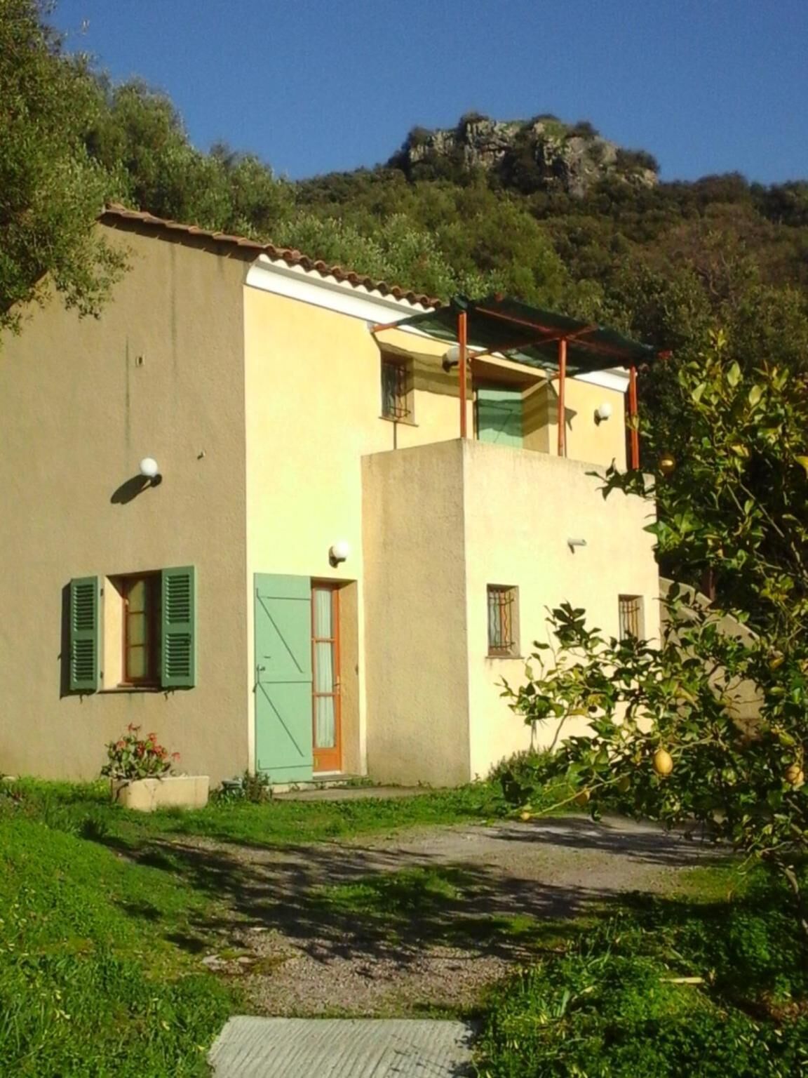 A two-story building with a flat roof, a balcony, and a door with green shutters.