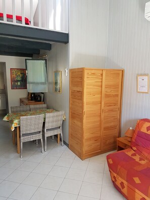 Un espace de vie compact comprenant une table à manger, des chaises en osier, une armoire en bois et un canapé.