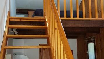 Una escalera de madera que conduce a un dormitorio en buhardilla con una cama litera.