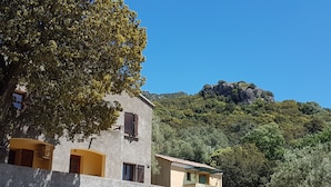 Um edifício de dois andares com fachada de pedra, um letreiro indicando uma casa com quartos e vista para uma encosta arborizada.