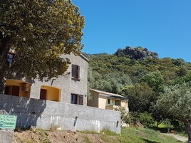 Un edificio de dos pisos con fachada de piedra, un letrero que indica una casa con habitaciones y vistas a una ladera boscosa.