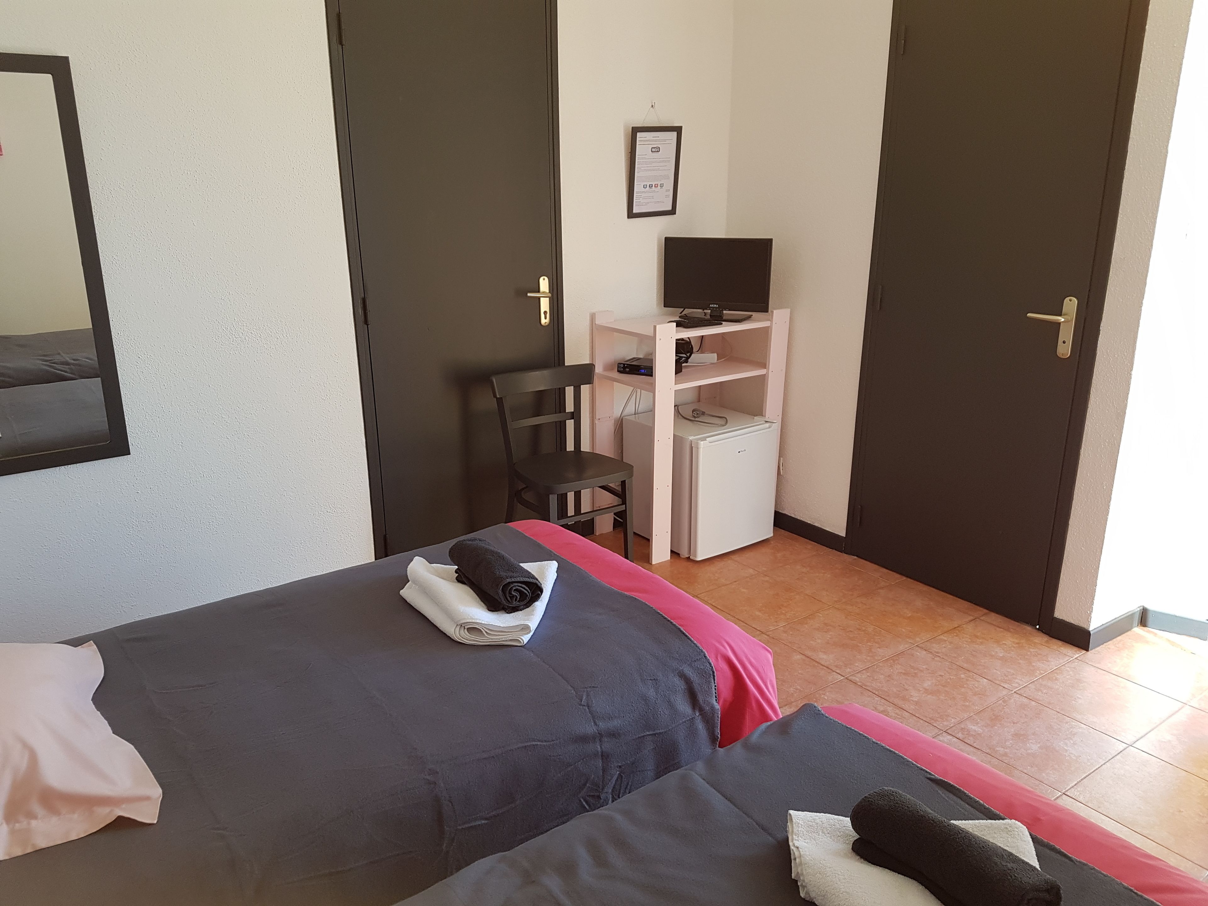A hotel room with two beds, a desk with a computer, a chair, and a small refrigerator.