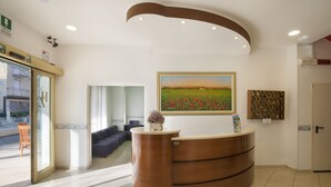A reception area with a curved wooden desk, a framed painting of a field, and a wall-mounted display of keys. - Hotel Zamagna (Cesenatico)