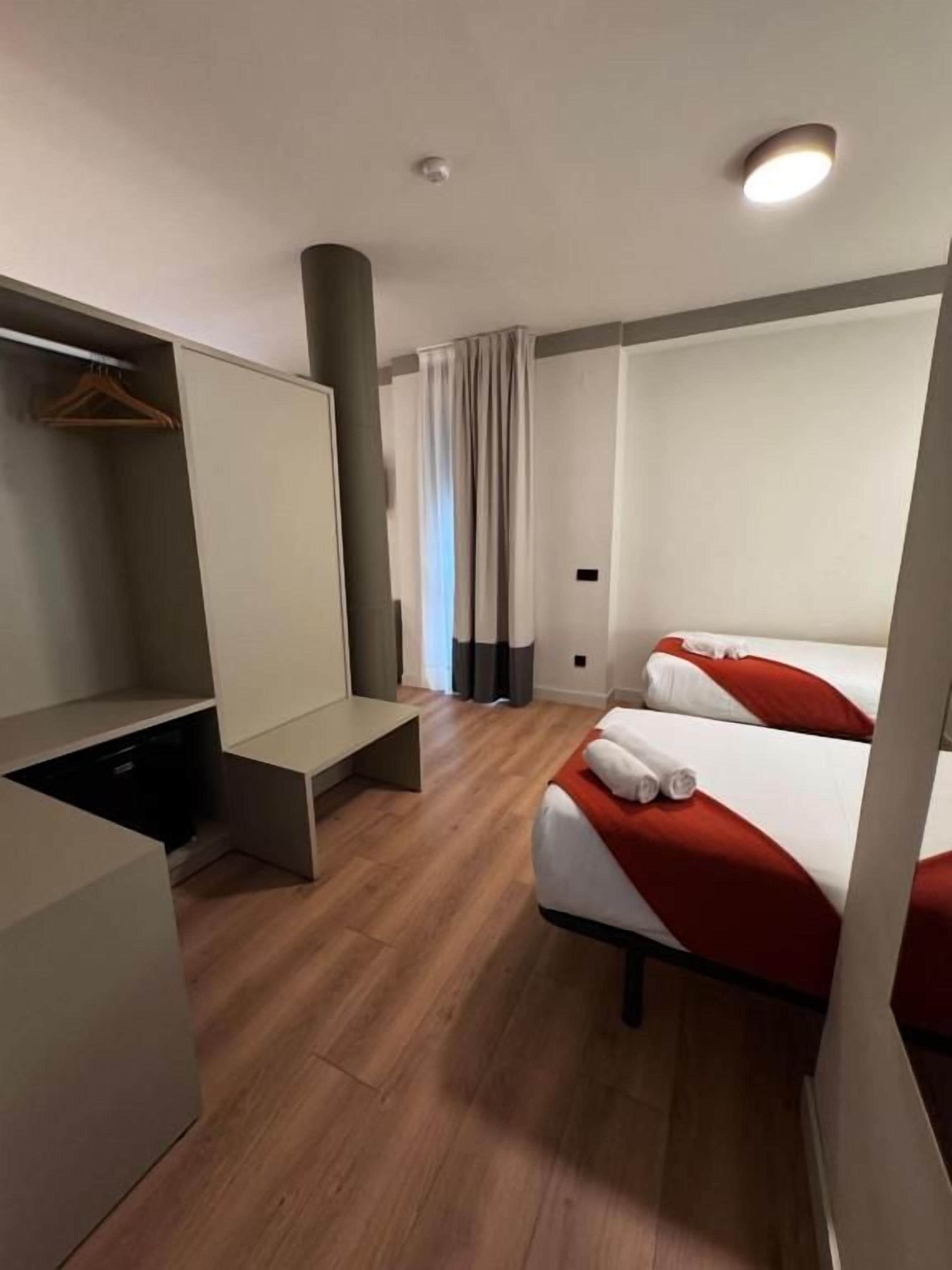 Une chambre d’hôtel avec un lit, un bureau, une armoire et une fenêtre avec des rideaux.