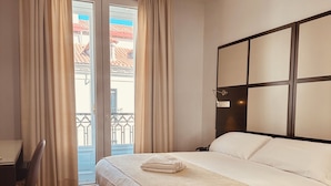 A hotel room with a bed, a desk, a chair, and a balcony with curtains. - Hostal Sol Square Madrid (Madrid)
