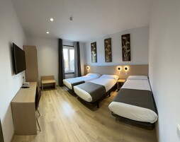 A hotel room with two single beds, a desk with a TV, and a window with curtains.