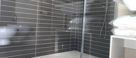 A modern bathroom with a glass-enclosed shower, dark tiled walls, and a white sink area.