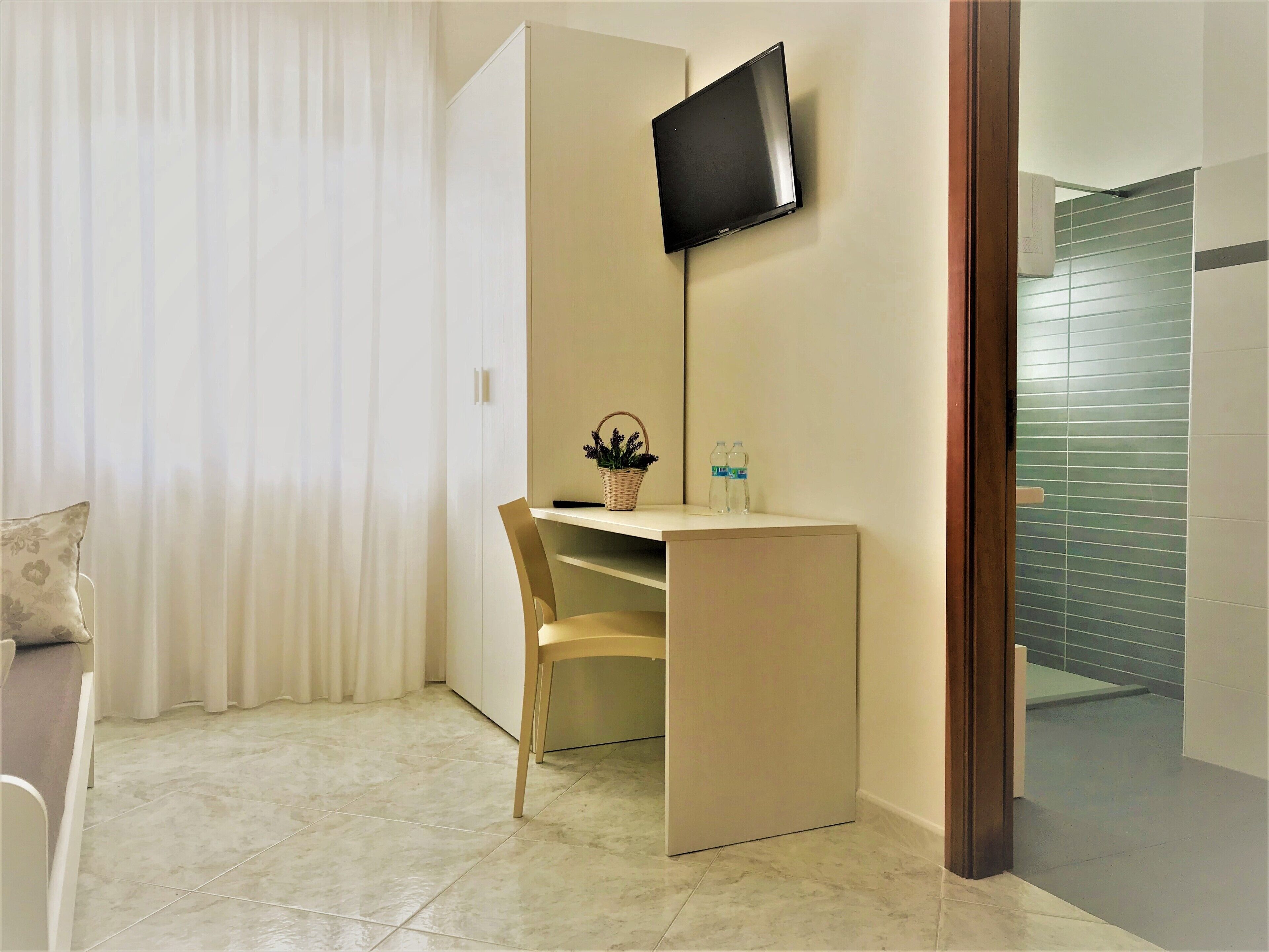 A hotel room with a desk, chair, TV, and a view of the bathroom.
