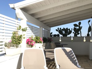 A covered outdoor seating area with white chairs and planters with flowers. - Innsud - Salentobedrooms (Nardò)