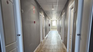 A long, narrow hallway with wooden flooring and white doors on both sides, leading to individual rooms.