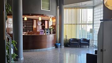 A spacious lobby with a reception desk, seating area, and large windows with blinds.