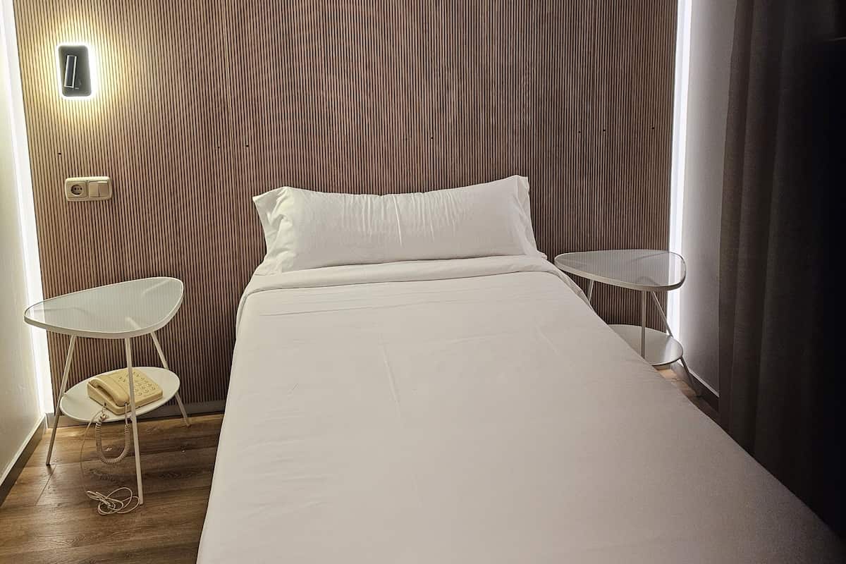 A modern hotel room with a large bed, a small table, and a wall-mounted light fixture.