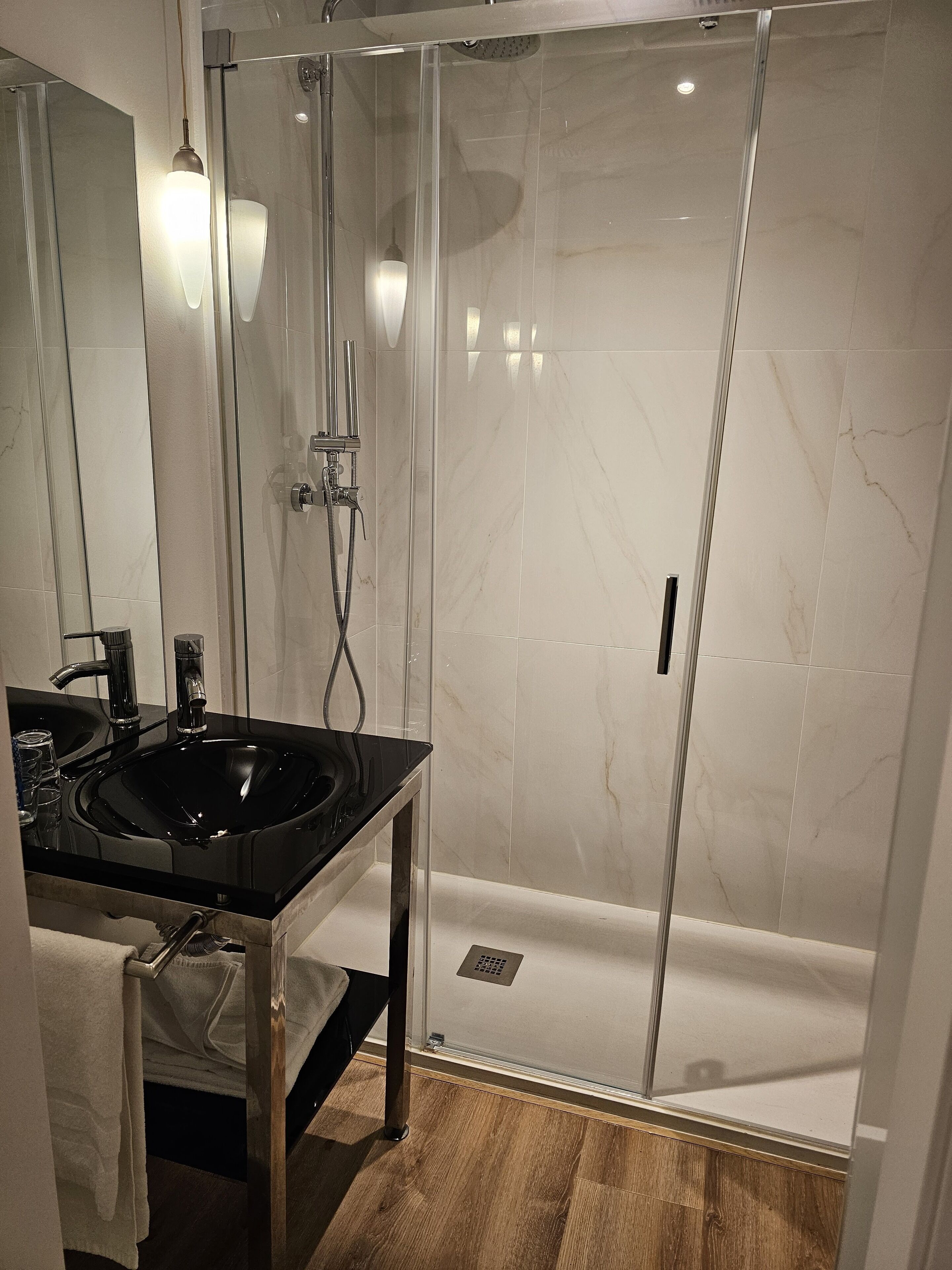 A modern bathroom with a glass-enclosed shower, a black sink, and a mirror.