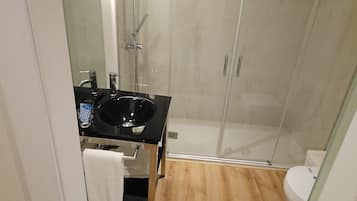 Un baño moderno con ducha de vidrio, un lavabo negro y suelo de madera.