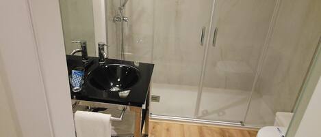 A modern bathroom with a glass-enclosed shower, a black sink, and a wooden floor.