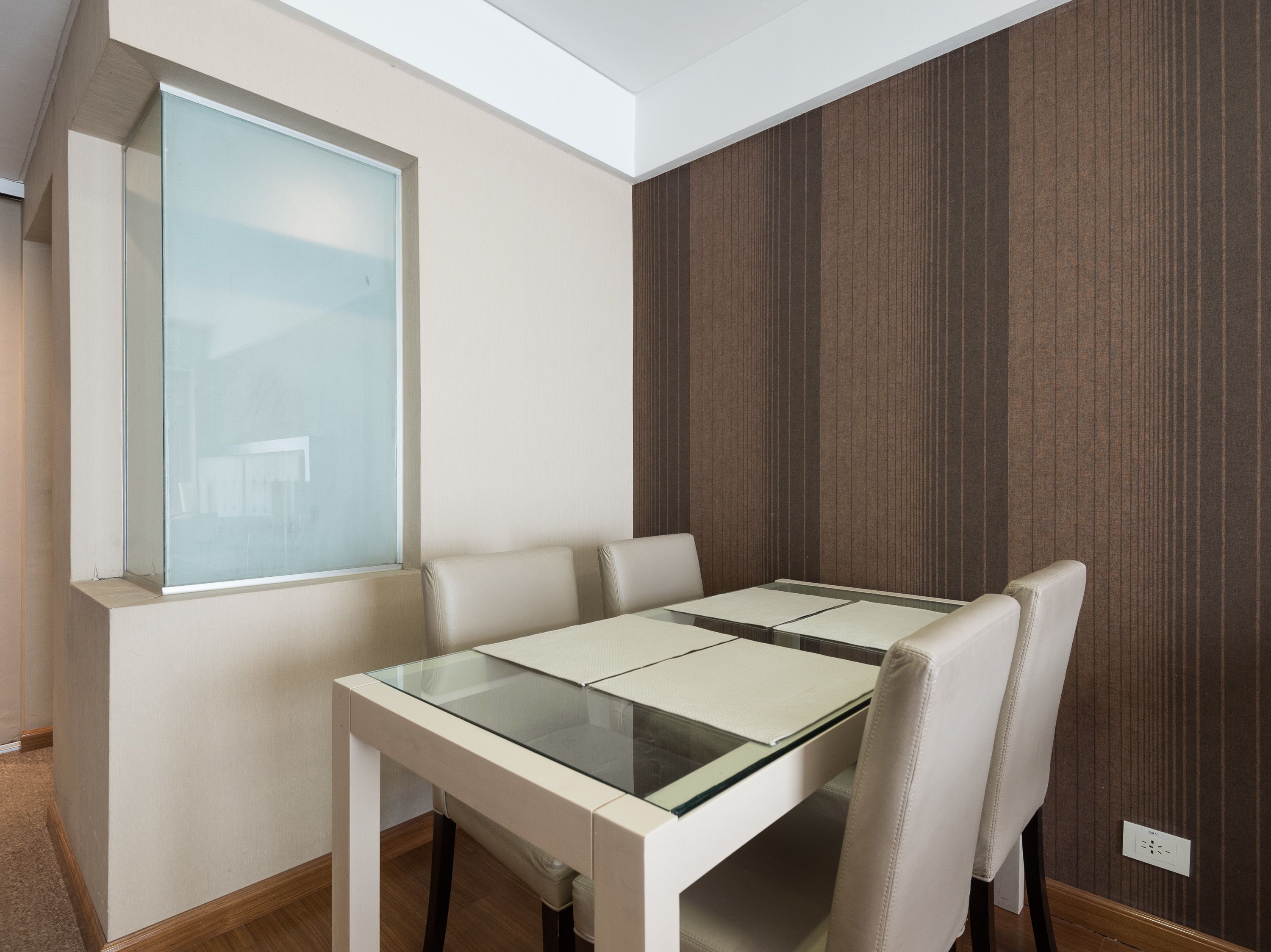 Un espace repas moderne avec une table à plateau en verre, quatre chaises et une grande fenêtre.