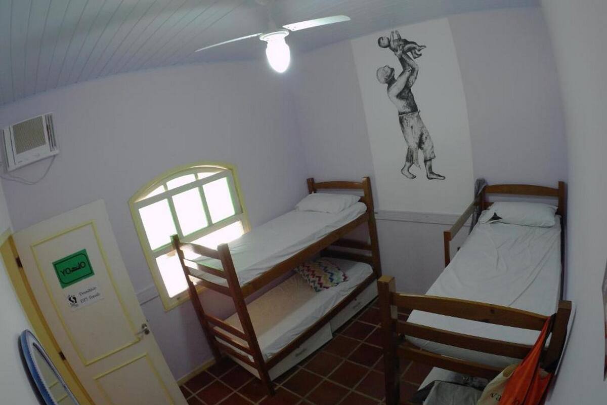 Une chambre de dortoir avec deux lits superposés, une fenêtre donnant sur un paysage agréable, un ventilateur de plafond et une fresque murale.
