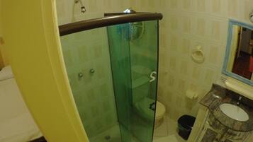 Un baño con cabina de ducha de vidrio, inodoro y lavamanos con espejo.