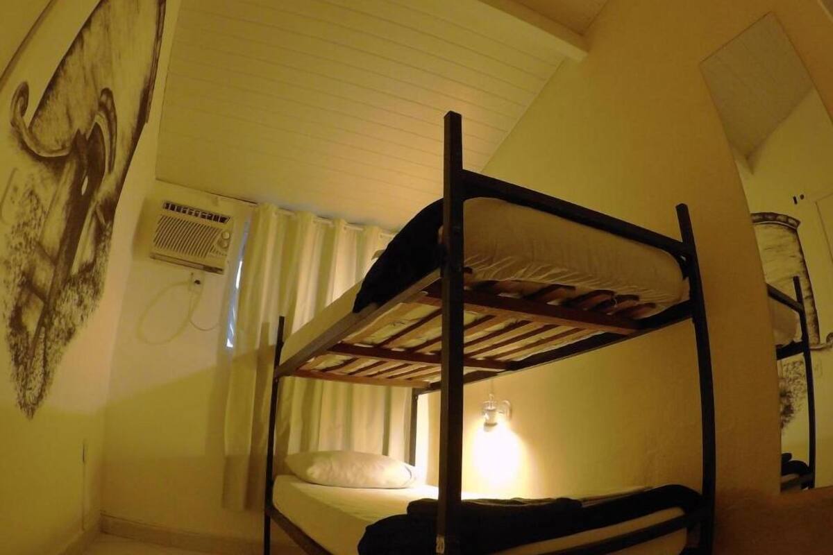 Une chambre avec un lit superposé, un ventilateur de plafond, un radiateur et un climatiseur fixé au mur.