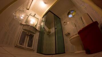 Un baño con cabina de ducha de vidrio, un inodoro y un cubo de basura rojo.