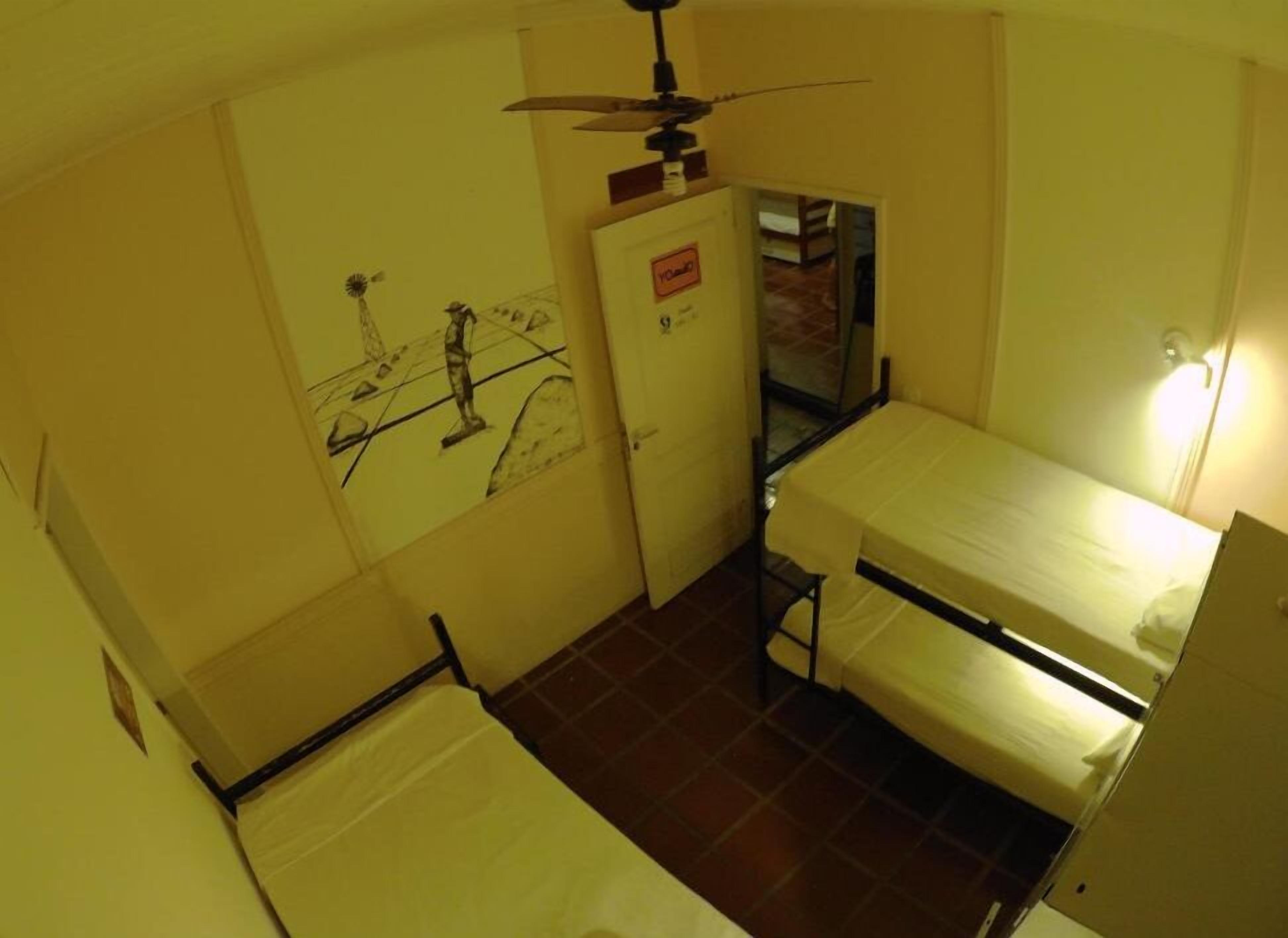 Una habitación pequeña y funcional con una cama litera, un ventilador de techo y una puerta con un cartel.