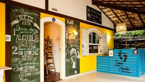Interior de un albergue juvenil con reglas escritas en una pizarra, una recepción y una escalera que sube a una habitación.