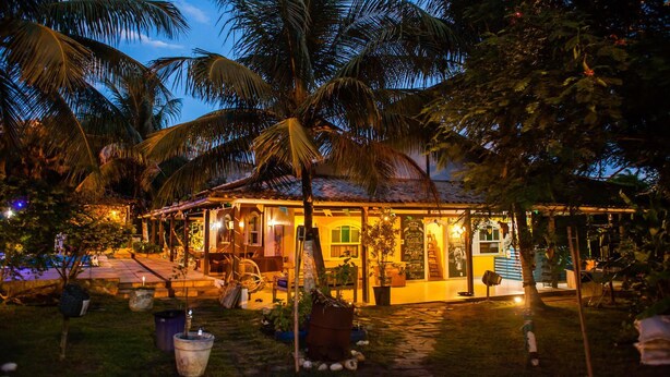 Un edificio bien iluminado de estilo tropical, con un porche cubierto y área de estar al aire libre, rodeado de palmeras.