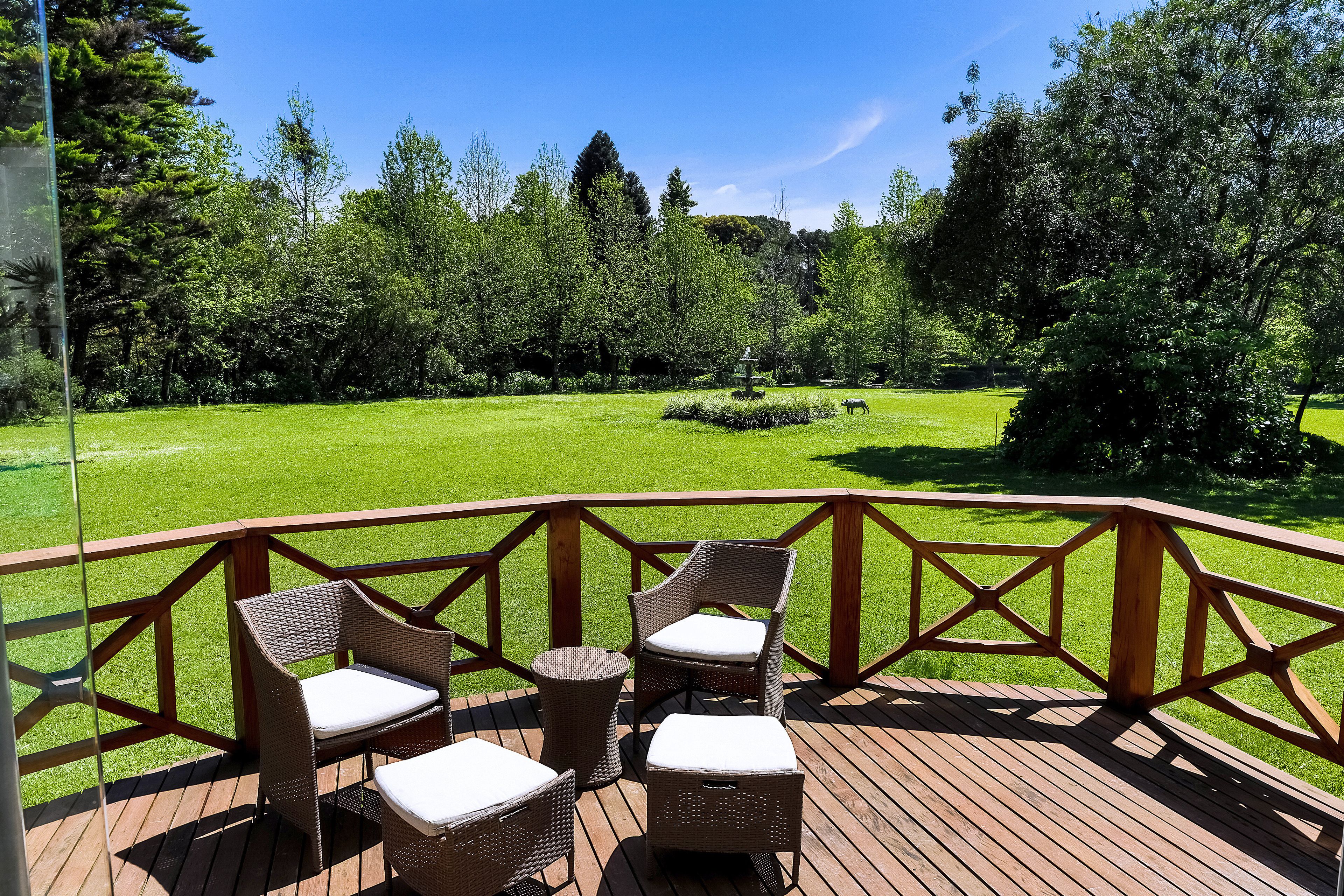 Eine Holzterrasse mit Korbmöbeln und Blick auf eine grüne Wiese und Bäume.