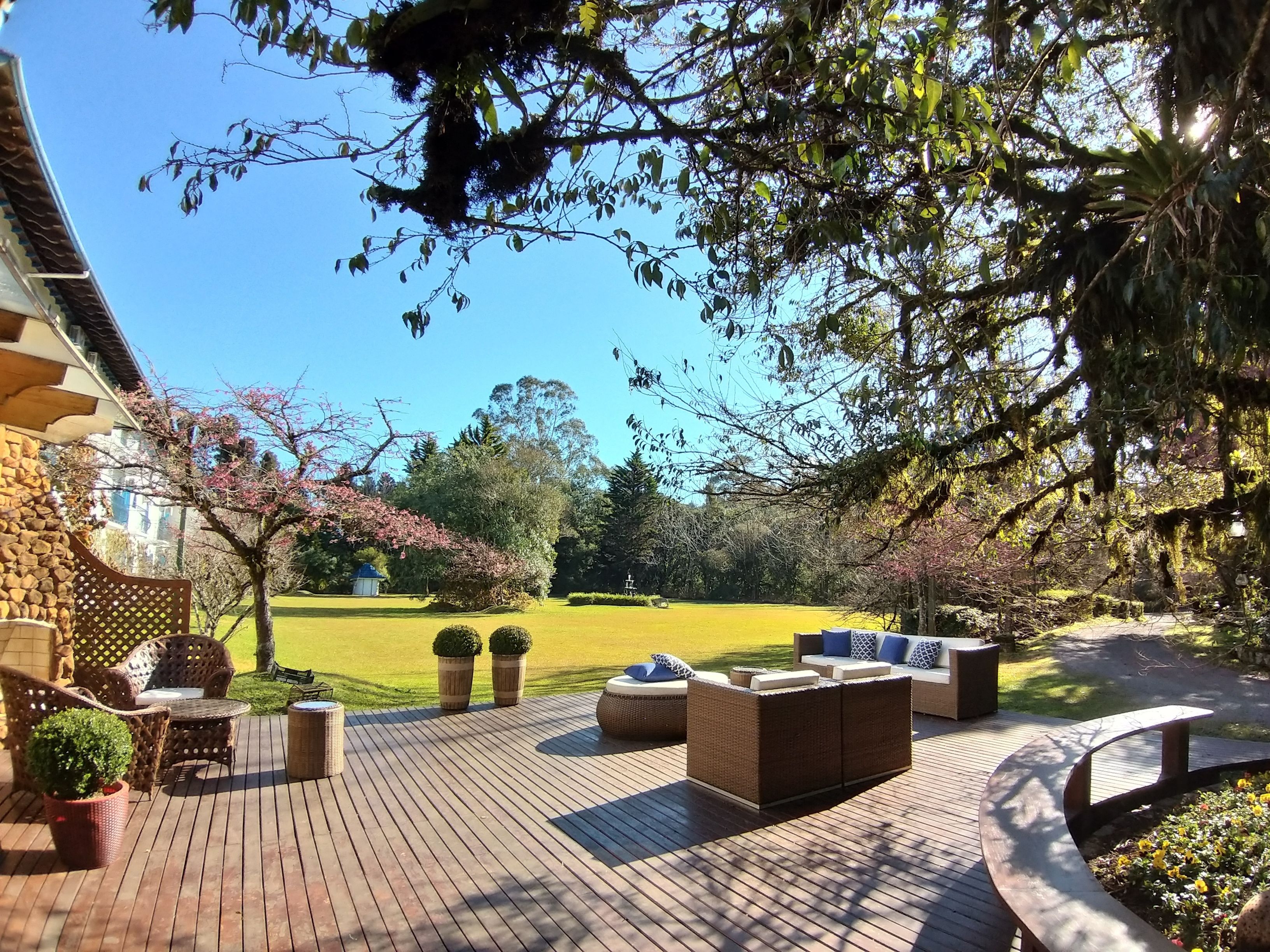 Un patio con mobiliario de mimbre, una pared de piedra y vistas a un jardín con césped y árboles.