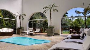 A modern indoor pool area with lounge chairs, a small pool, and large windows offering views of greenery.