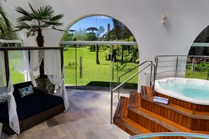 A modern outdoor relaxation area with a wooden hot tub, a cushioned seating area with a canopy, and a view of a well-maintained garden. - Hotel Gramado Palace (Gramado)