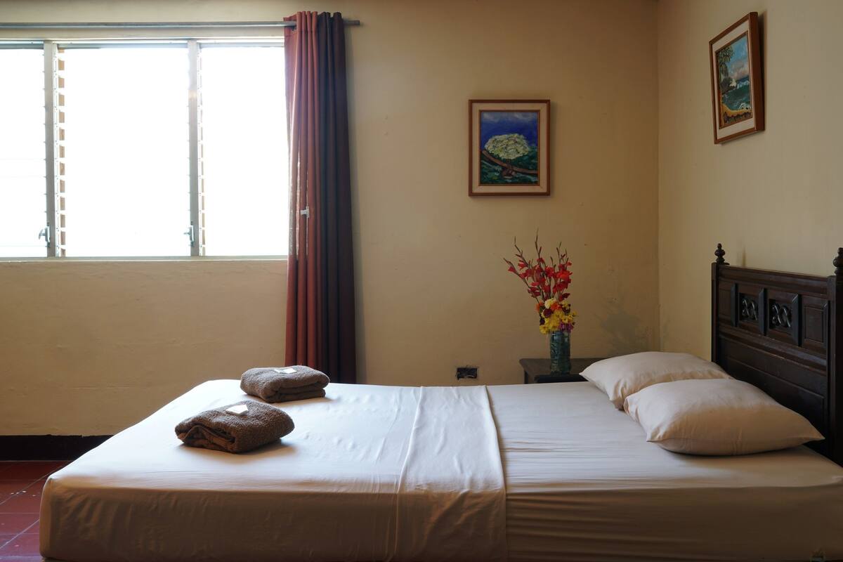 Une chambre d’hôtel avec un lit, des oreillers, un vase de fleurs et un tableau au mur.
