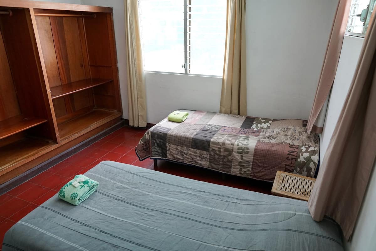 Une chambre avec deux lits, une armoire en bois et une fenêtre avec des rideaux.