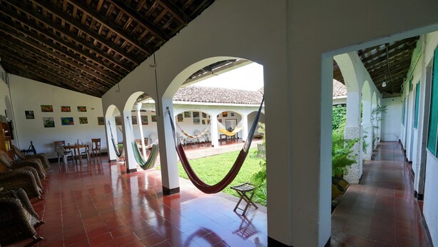 A covered corridor with a tiled floor, hammocks, and a view of a courtyard with a tiled roof and greenery. - El Arca de Noé Lodging (Granada)