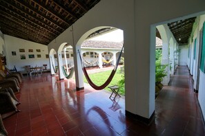 A covered corridor with a tiled floor, hammocks, and a view of a courtyard with a tiled roof and greenery. - El Arca de Noé Lodging (Granada)