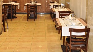 Un restaurante con varias mesas, sillas de madera y suelo de baldosas.