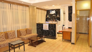 Vestíbulo de hotel con sofás, mostrador de recepción, televisor y zona de bar.
