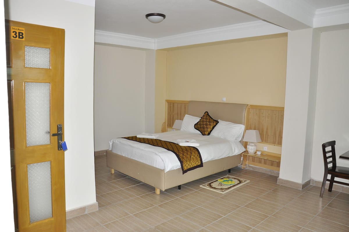 Une chambre d’hôtel comprenant un lit, une table de chevet, une chaise et une porte dont les panneaux sont en verre dépoli.