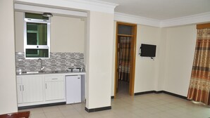 Una cocina compacta con armarios blancos, un microondas integrado y una ventana con marco verde.