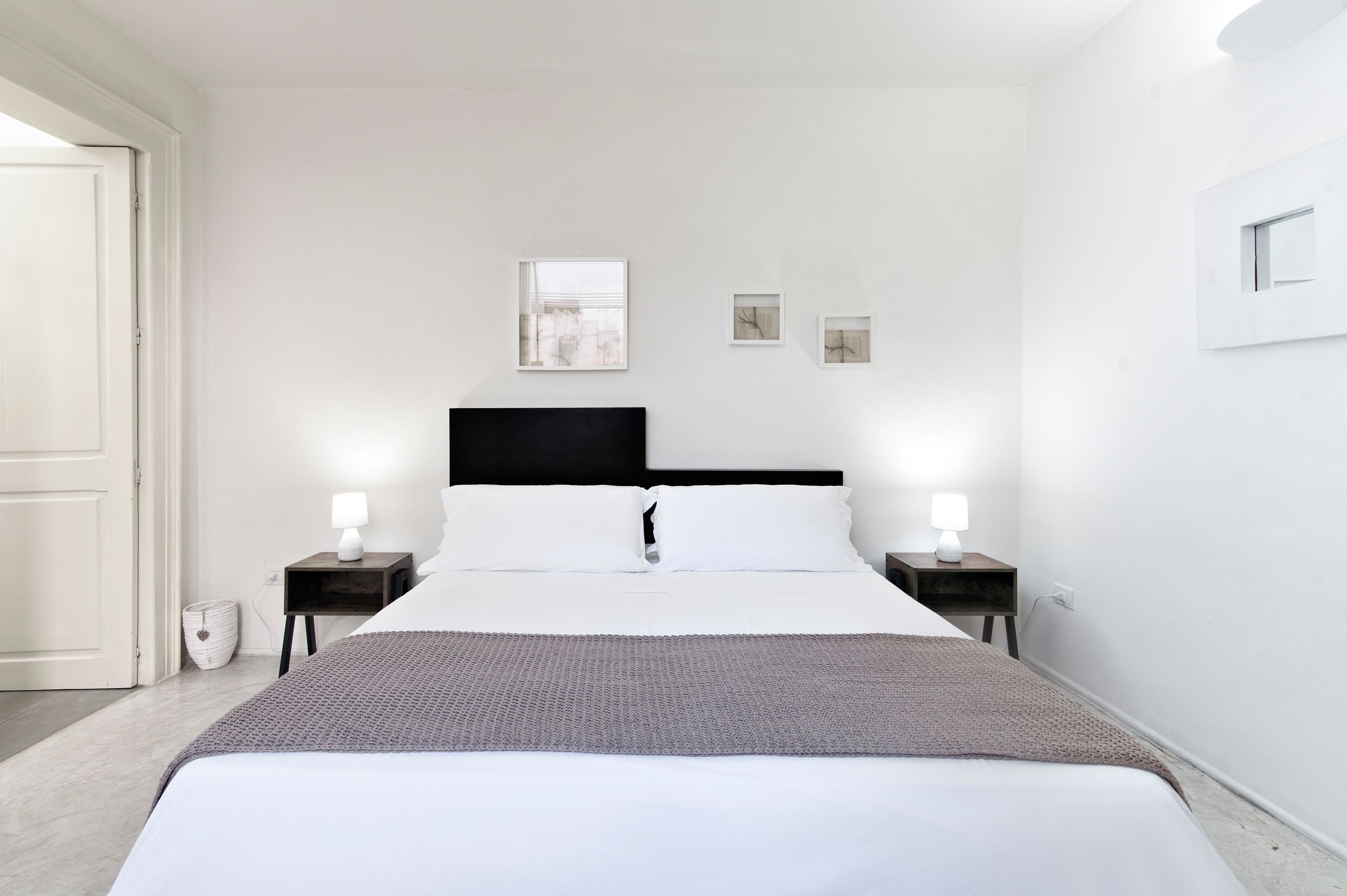 Een moderne slaapkamer met een groot bed, twee nachtkastjes met lampen, een zwart hoofdeinde en drie ingelijste foto's aan de muur.