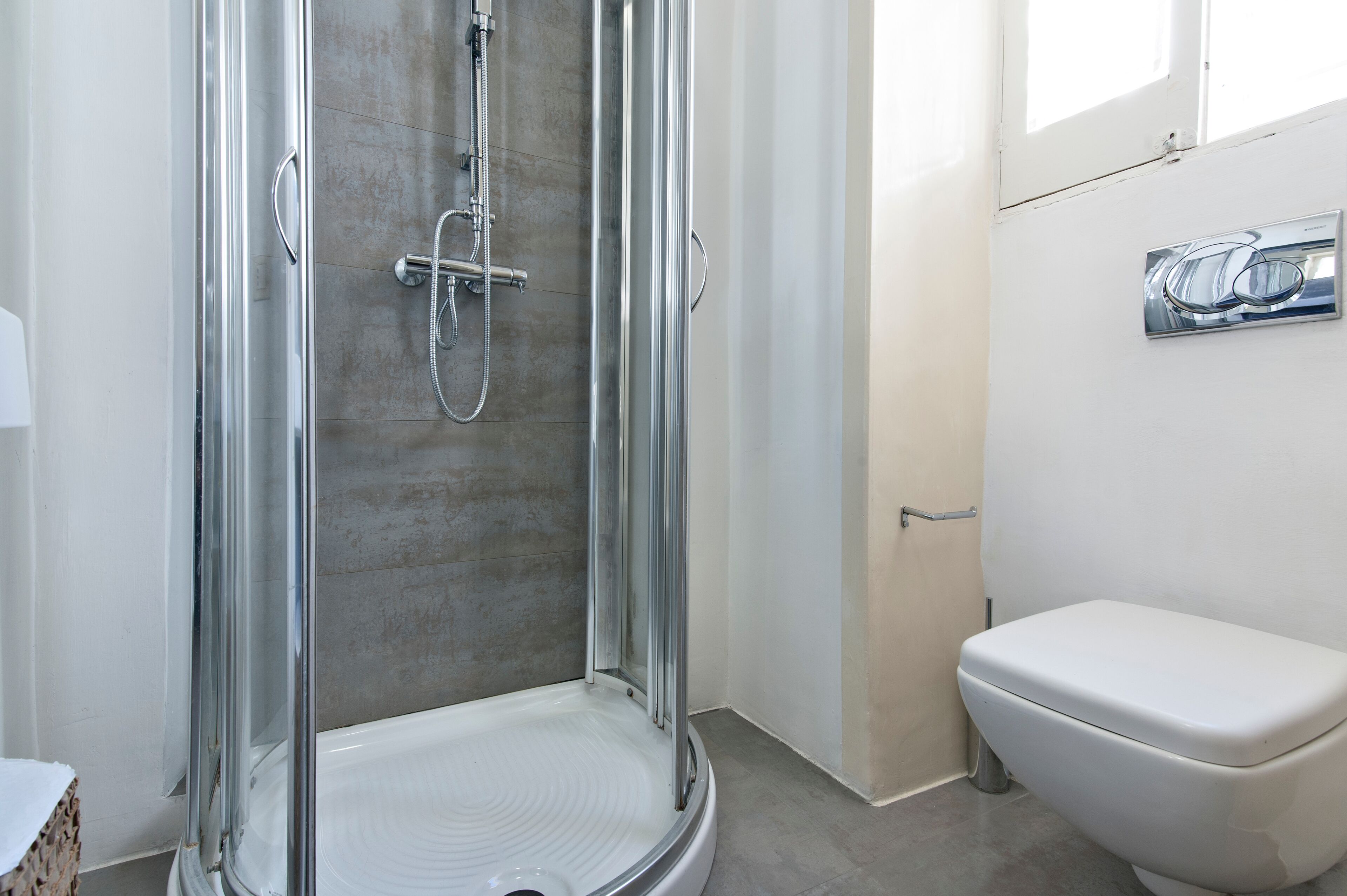 A modern bathroom with a glass-enclosed shower, a white toilet, and a visible water heater on the wall.