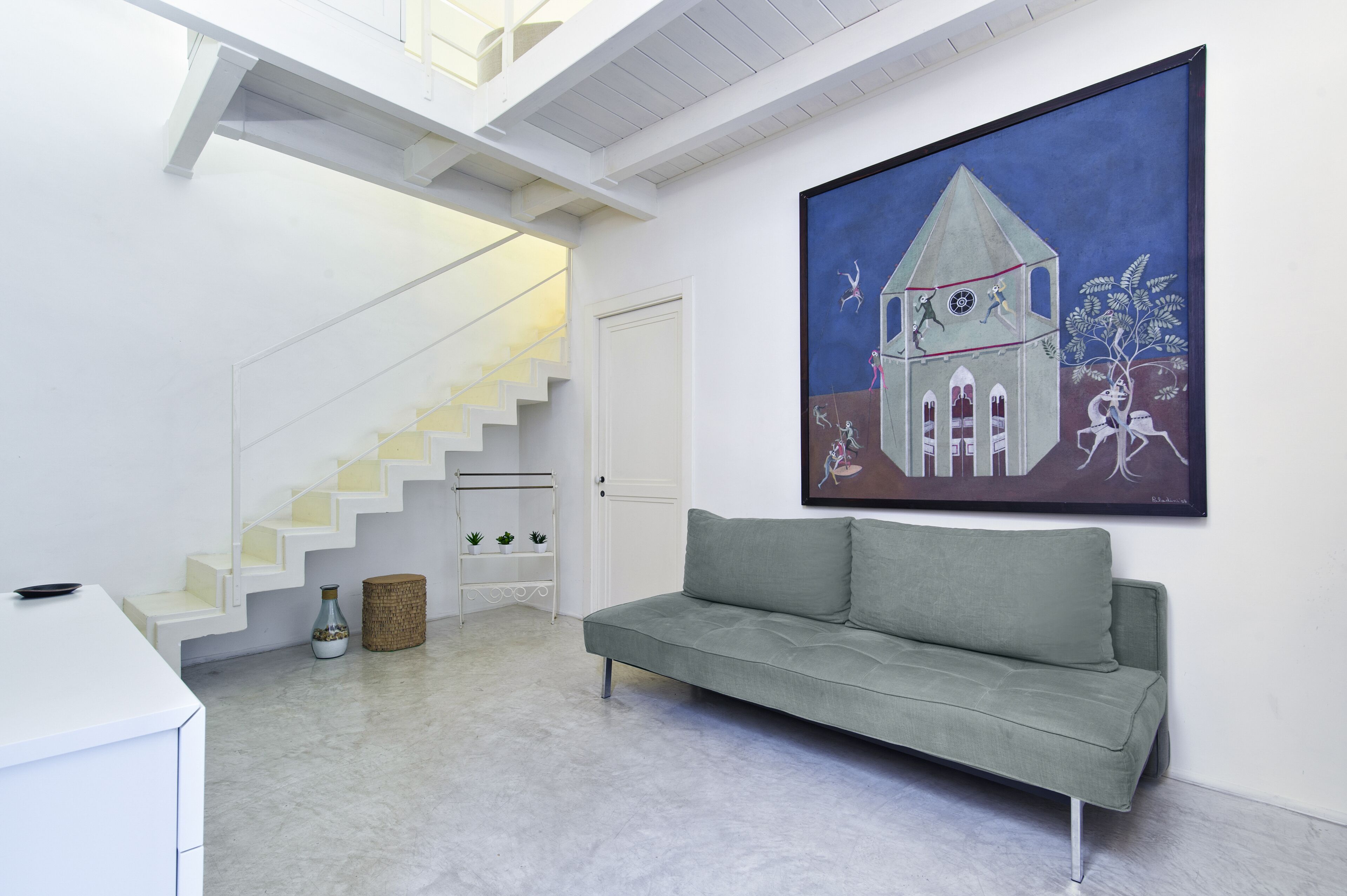 Un intérieur moderne avec un escalier, un canapé gris et un grand tableau abstrait accroché au mur.