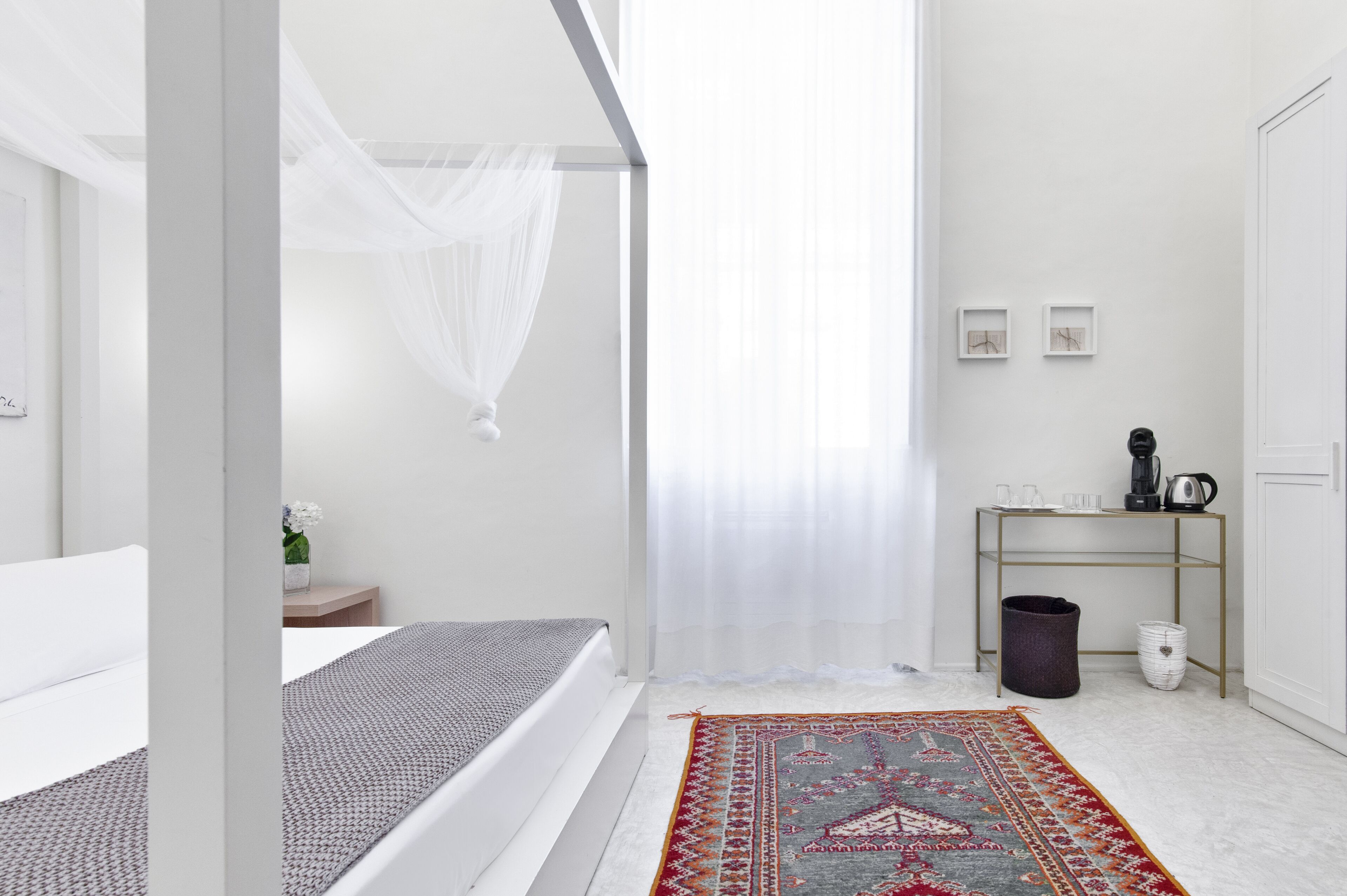 A modern bedroom with a bed, a bedside table, a small table with a kettle, and a trash bin.