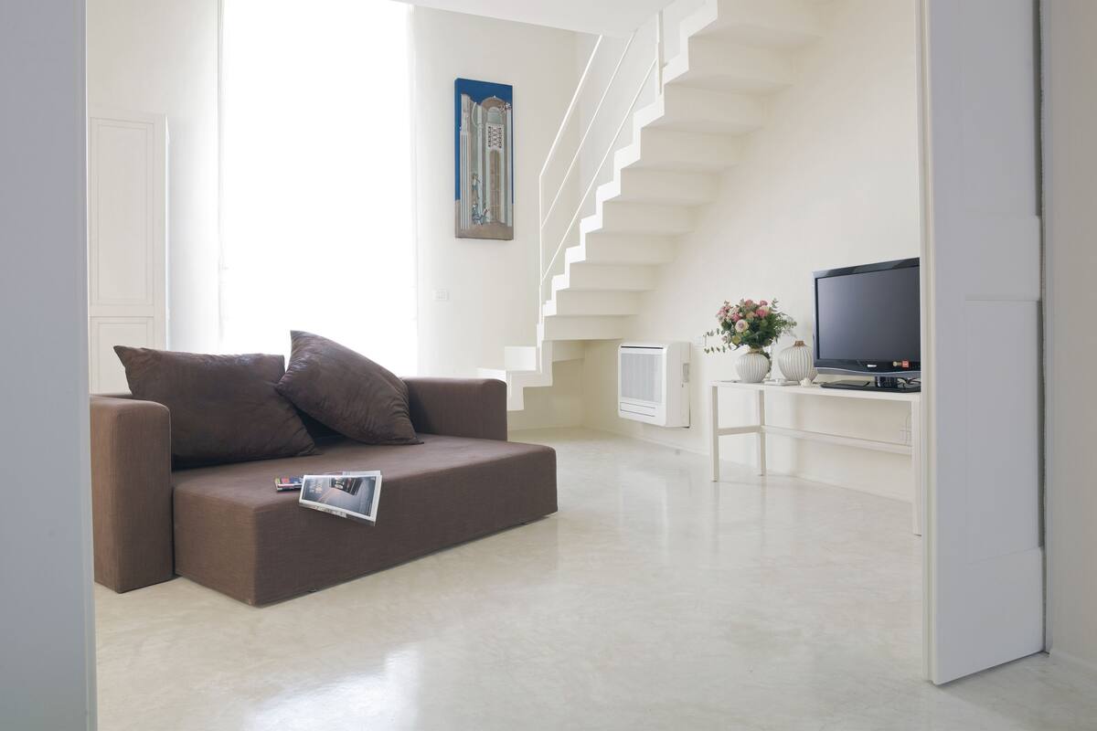 A modern living room with a brown sofa, a flat-screen TV, and a staircase leading to an upper floor.