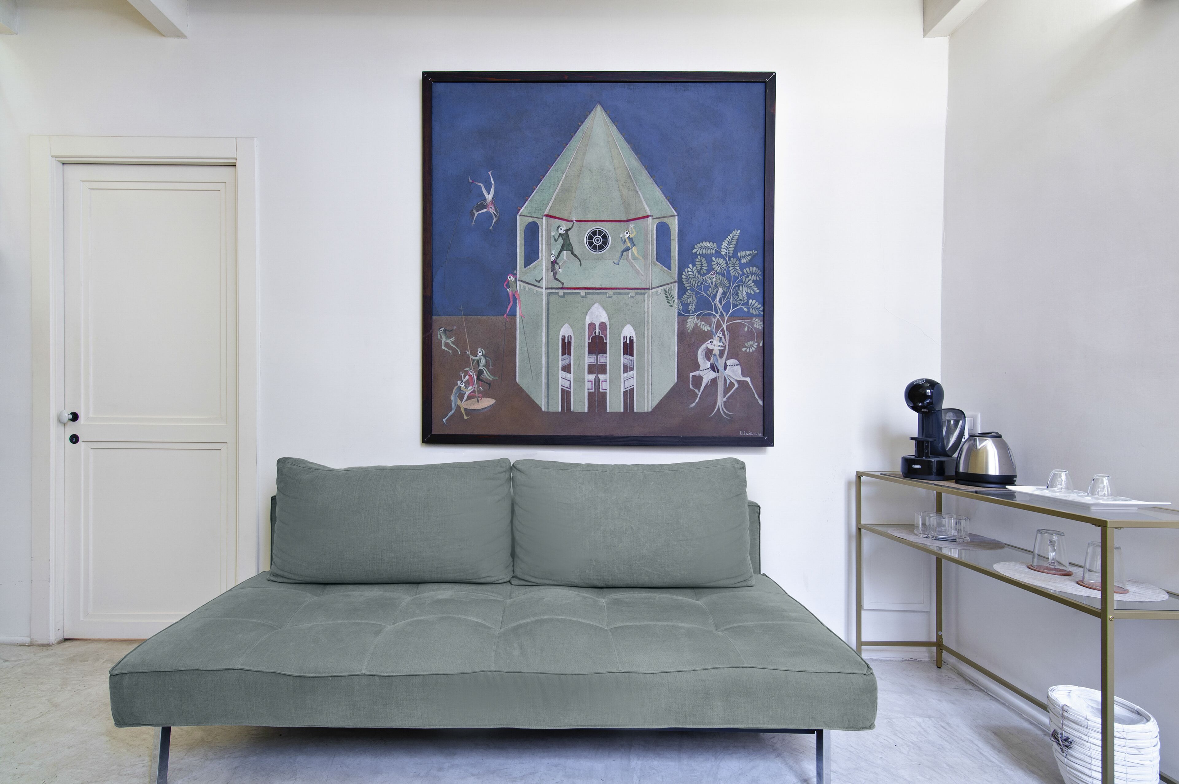 Una habitación con un sofá verde, una obra de arte enmarcada en la pared, una cafetera y una pequeña mesa con vasos.