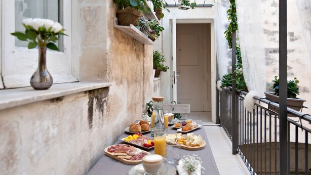 Un desayuno en un balcón con diversos alimentos, un florero con flores y plantas en macetas.
