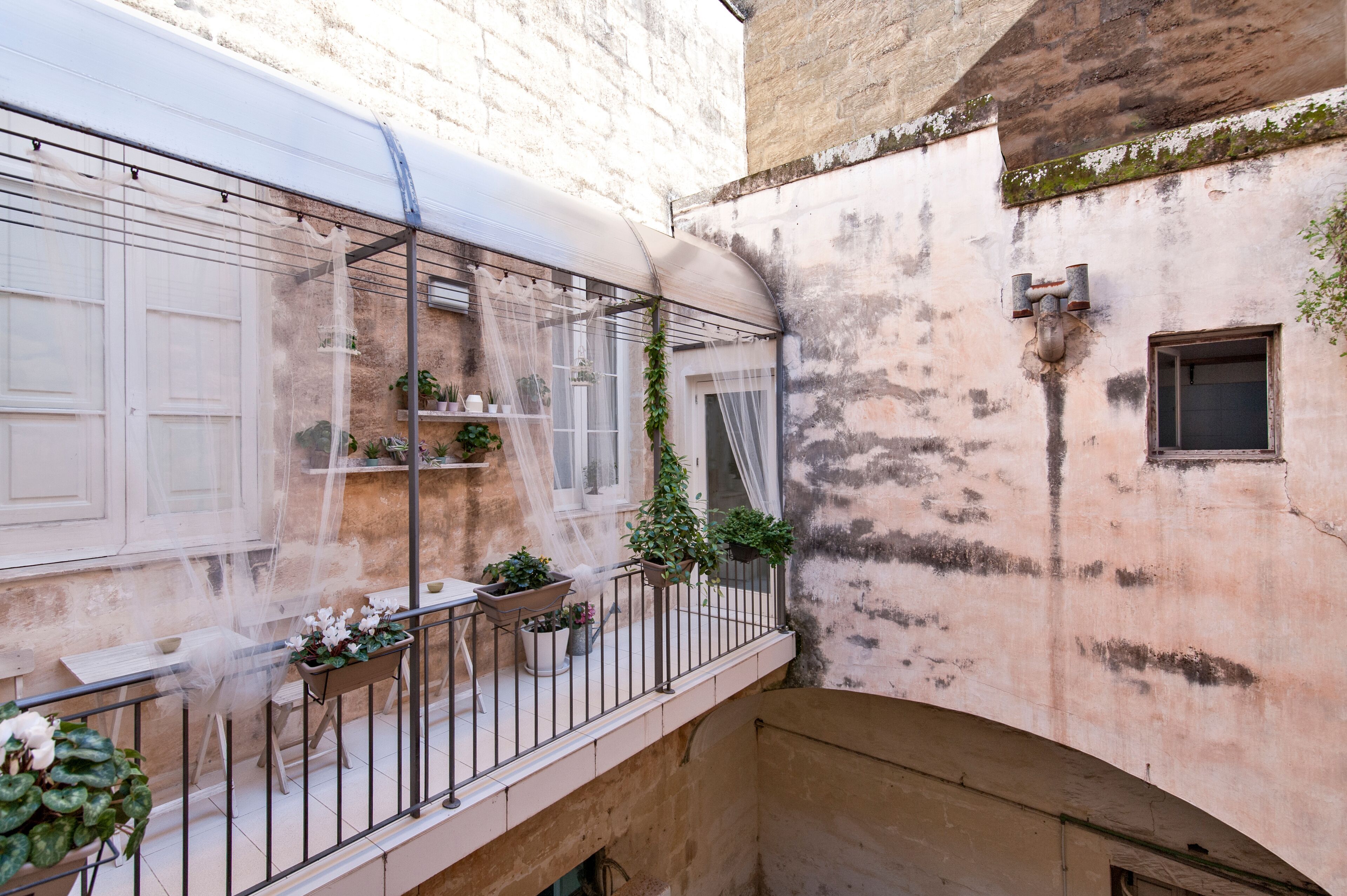 A courtyard with a covered balcony, potted plants, and a rustic building facade.